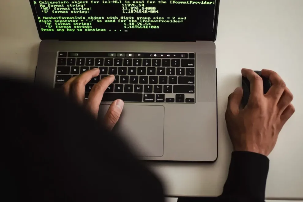 ataques-ciberneticos-any-consulting-pexels-sora-shimazaki-5926393 em primeiro plano, o capuz de um moletom desfocado. Depois, um computador da Apple sendo usado pela pessoa do capuz com a tela mostramdo códigos que representam ataques cibernéticos.